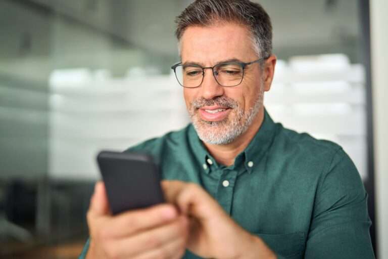 Busy smiling business man looking at phone working on mobile in office.