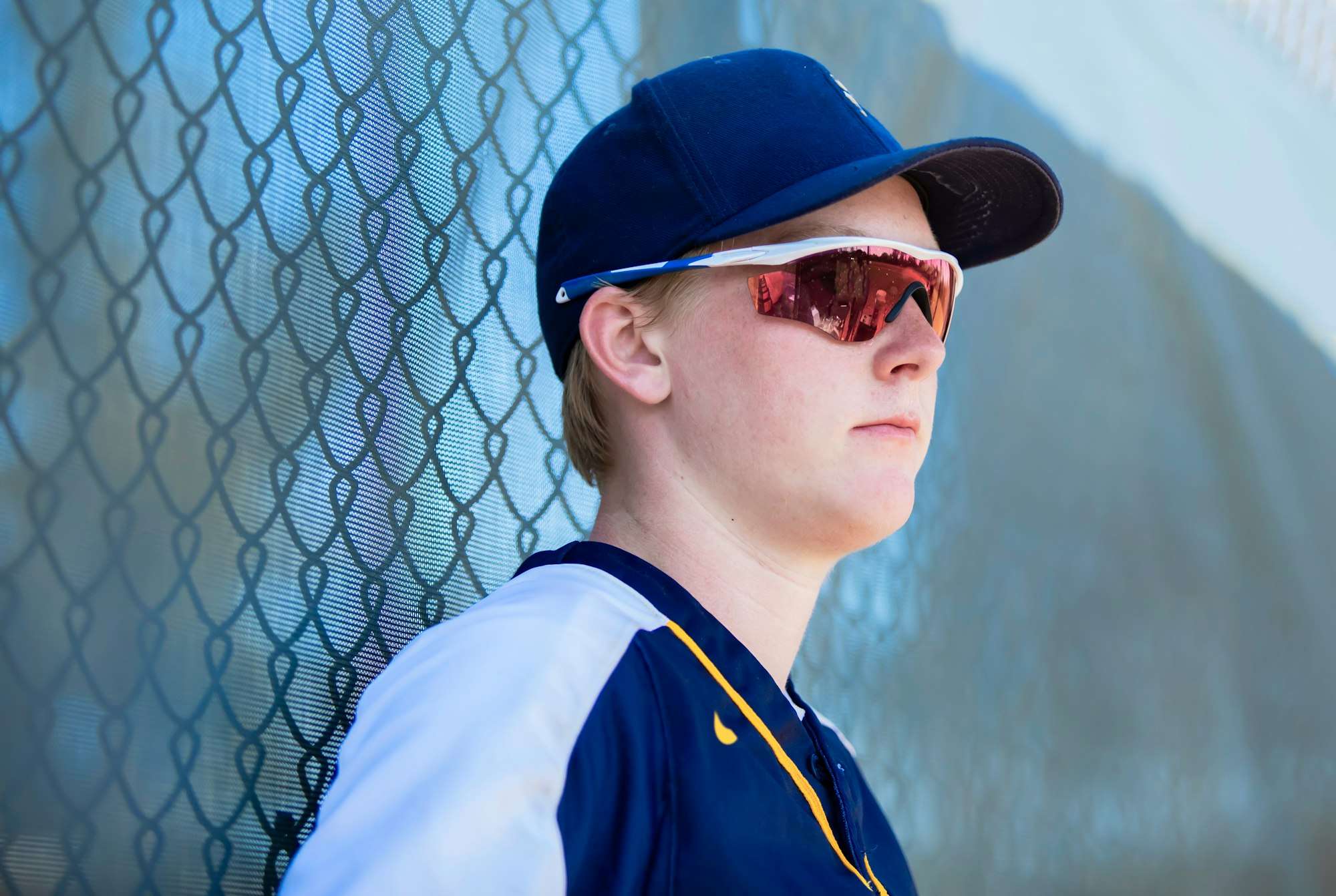 High school baseball player leaning against the fence wearing cap and sunglasses