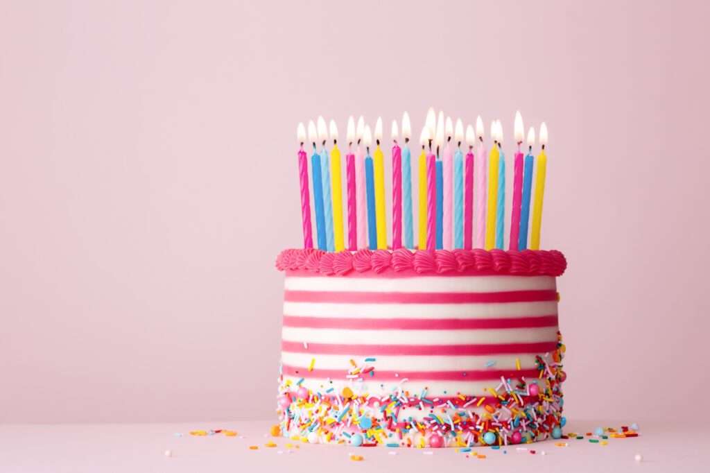 Pink and white striped birthday cake with lots of candles