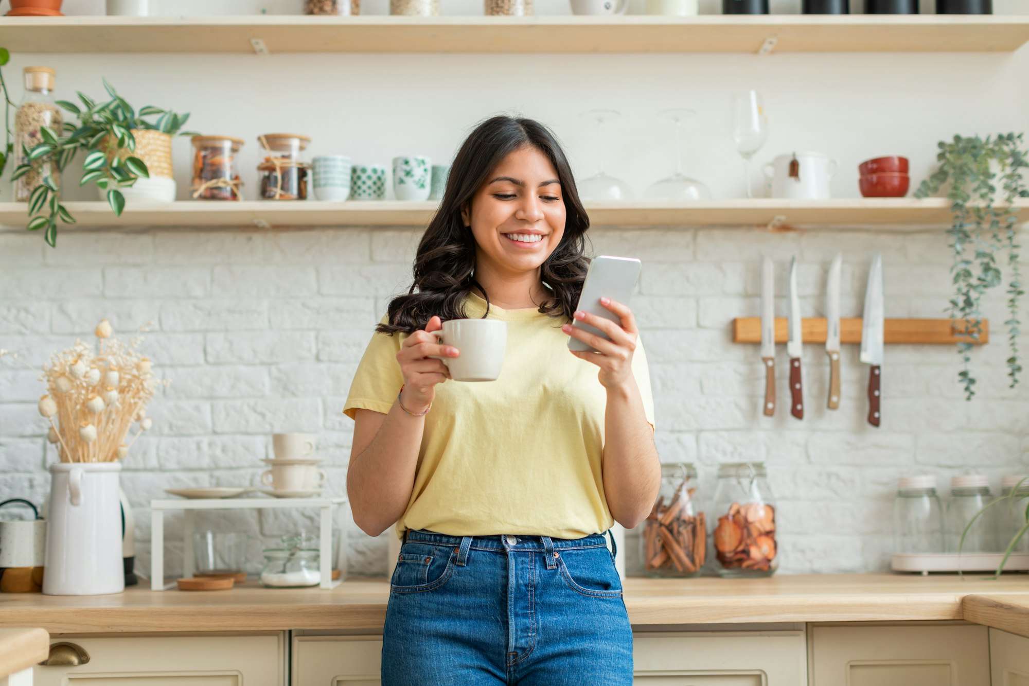 Woman smiling with coffee and smartphone in kitchen